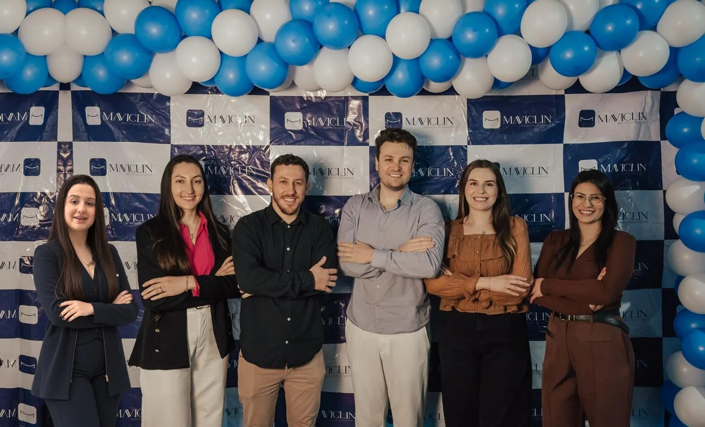 Os dentistas da Maviclin lado a lado, de braços cruzados, em frente ao painel da clínica